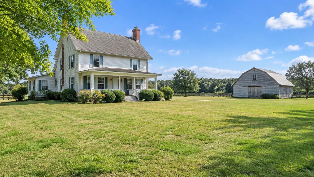 Older farmhouse on a large grassy lot with a detached barn under open sky in Landstown, Virginia Beach, Virginia